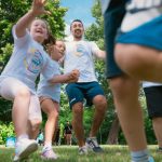 Joyful group of children and adult engaging in playful activities in a sunny park setting.